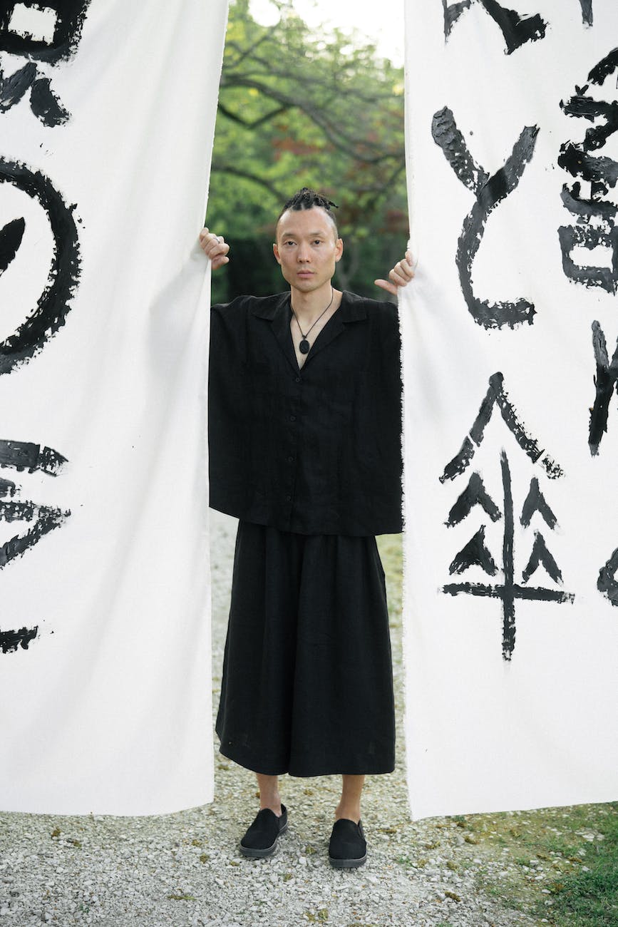 man in black yukata standing beside white textile with japanese calligraphy